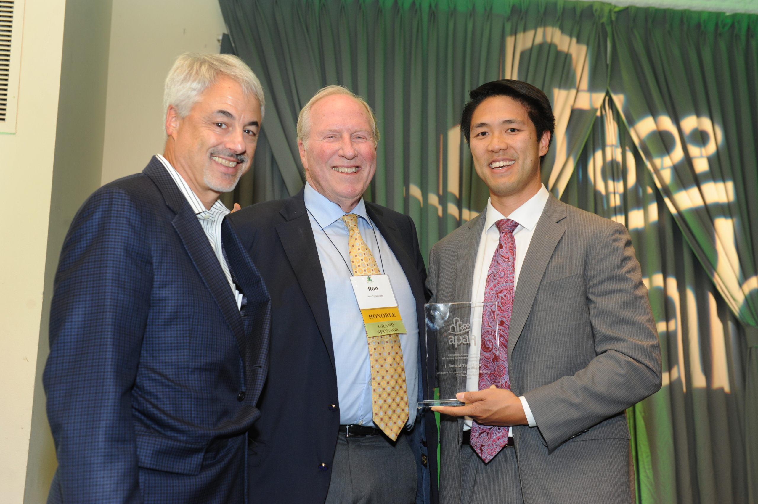 Three men posing with an award at a gala event
