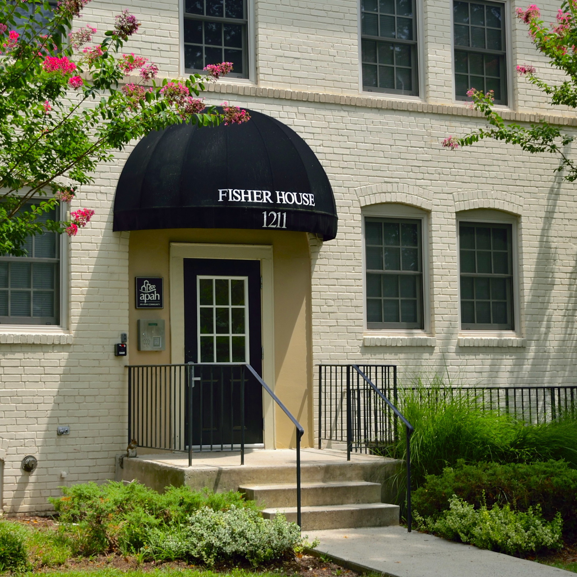 Fisher House building entrance with black awning and white brick walls.