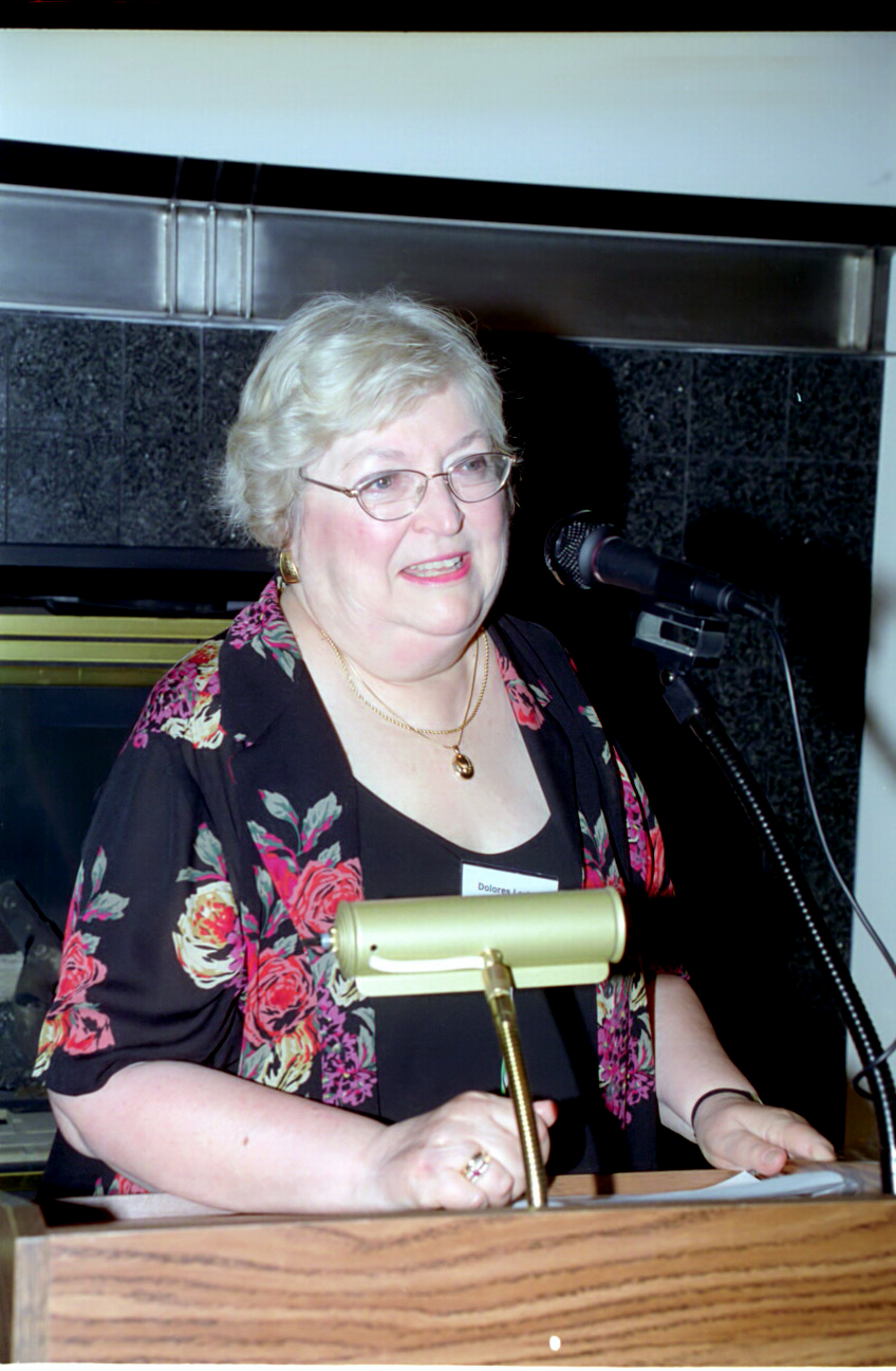 Dolores, wearing glasses, speaking in front of a microphone at a conference