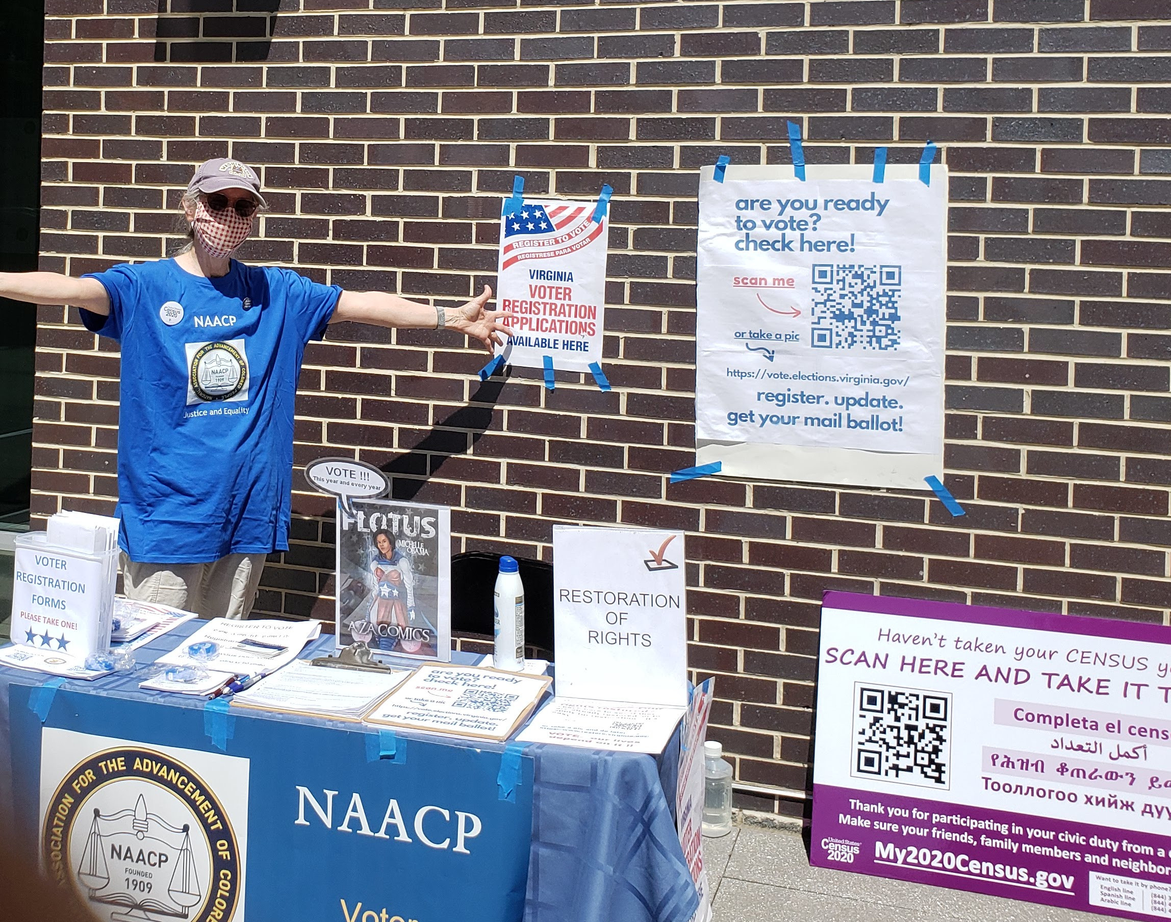 Volunteer dressed in a blue T-shirt, wearing a mask and glasses, with open arms.