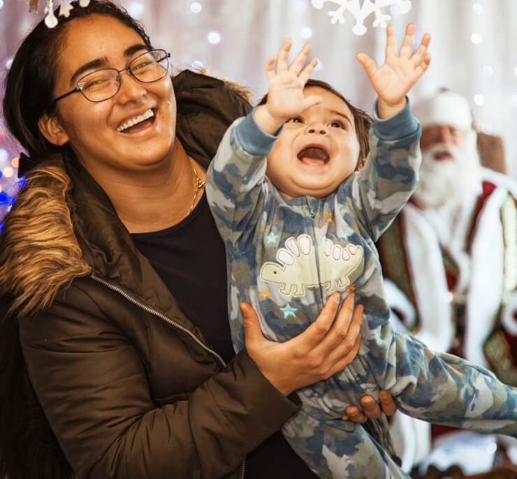 Mother holding her joyful baby who is reaching up, with holiday decorations in the background