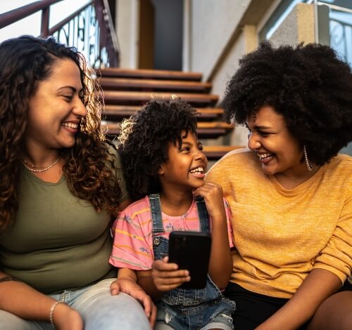 Mother and daughter smiling and sitting on stairs with a smartphone in hand