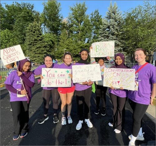 A group of people is standing together outdoors, smiling and holding motivational signs.