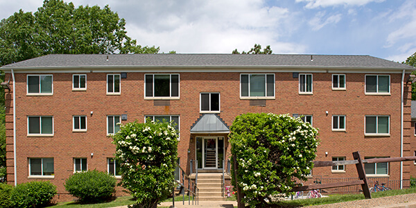 Two-story brick apartment with many windows, two shrubs, and a central entrance.