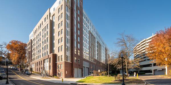 Modern multi-story building, sunny day; cars parked along the street, autumn-colored trees nearby.