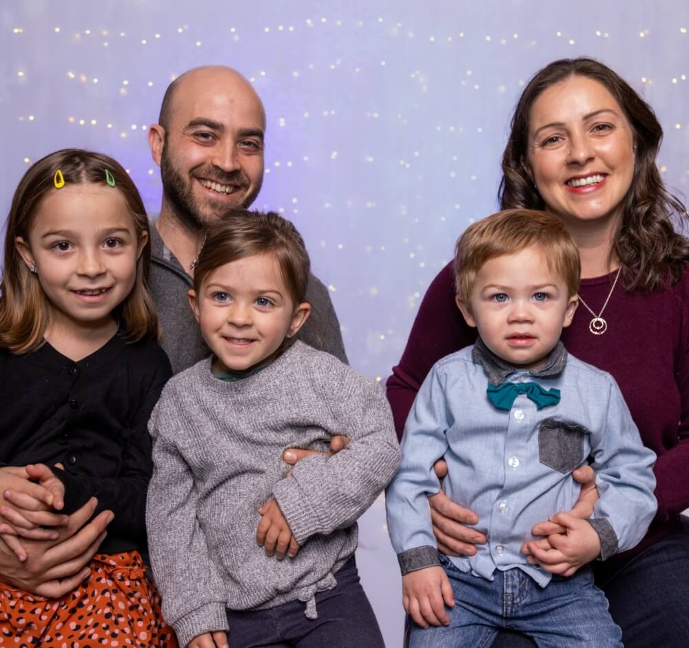 Family portrait with parents and three children smiling against a festive background