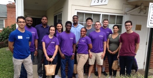 Group of volunteers in matching purple shirts posing outside a building.