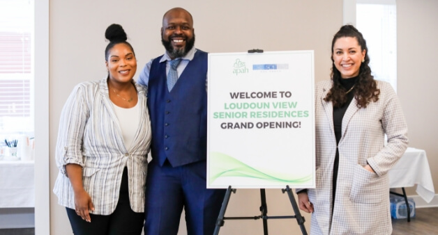 Three people smiling beside a sign that reads "Welcome to Loudoun View Senior Residences Grand Opening!