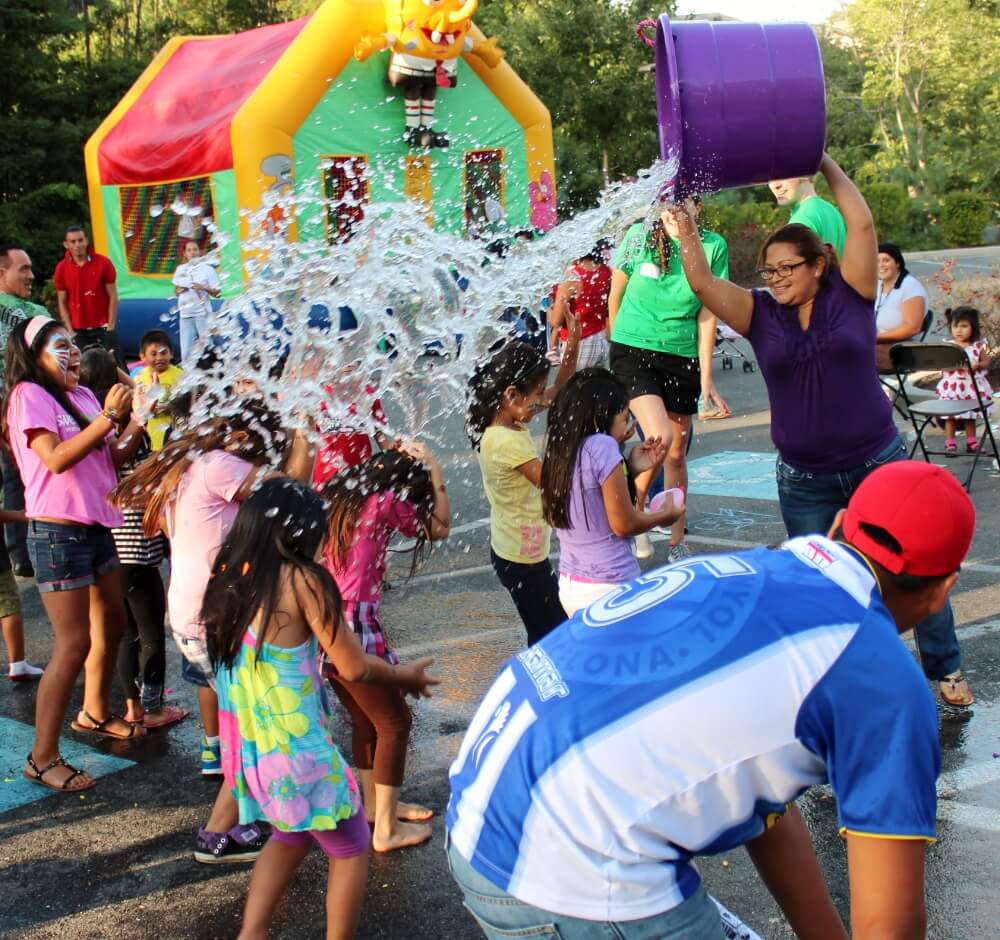 Children enjoying a water activity at a community event with a colorful inflatable in the background.