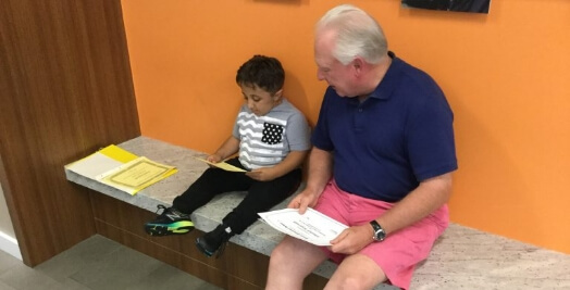 Adult and young boy sitting on a bench together, reading documents in a casual setting.