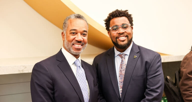 Two men in suits smiling at the camera during a professional event.