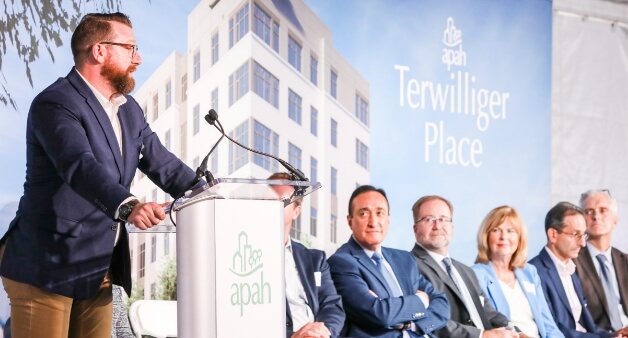 Speaker at podium addressing audience at Terwilliger Place event, with panelists seated behind.