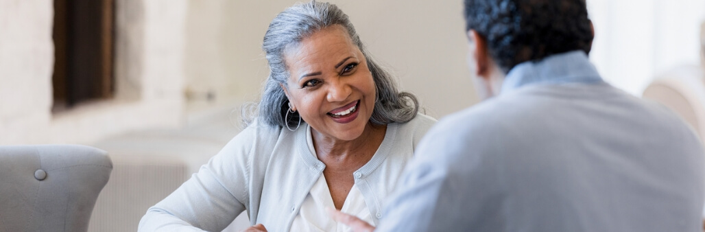 Smiling elderly woman engaging in conversation with another person at a table