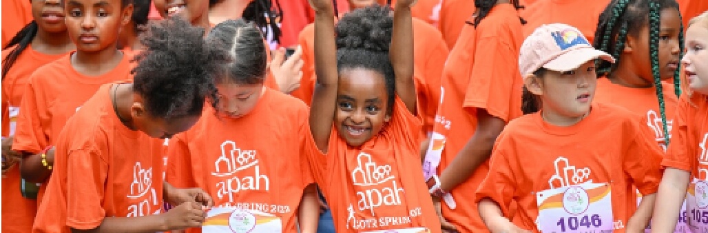 Group of excited children in matching orange APAH t-shirts at a community event.