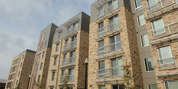 Modern brick and metal apartments with balconies stand near trees and a streetlamp—ideal for investors.