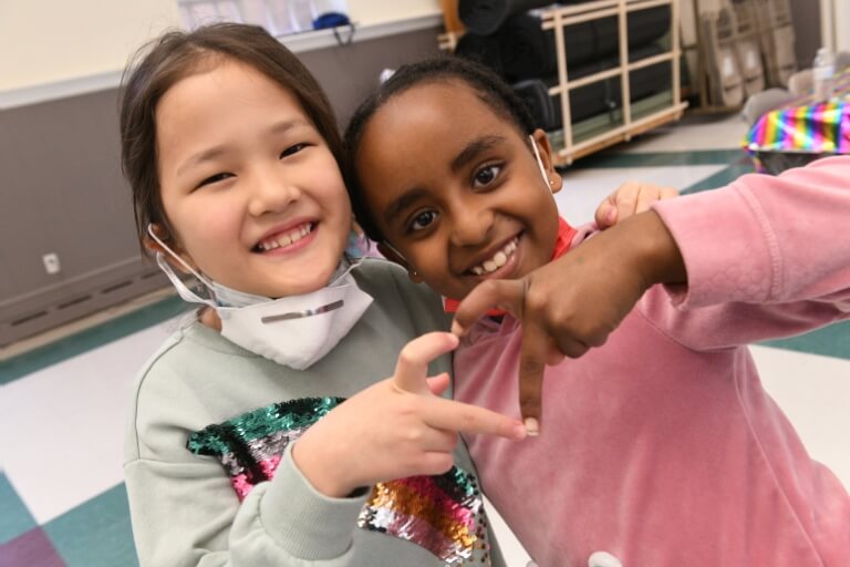 Two girls smiling and making a heart shape with their hands in a community center