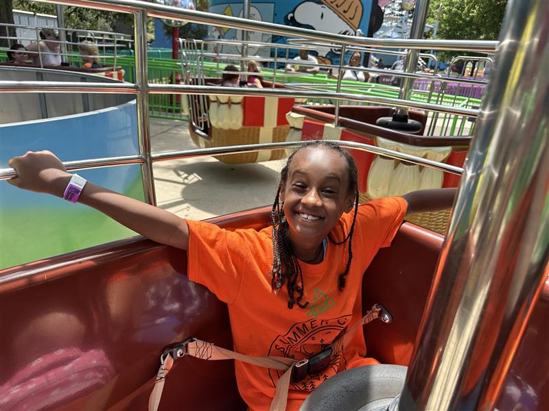 Girl smiling for the photo, wearing orange t-shirt, having fun in an amusement park